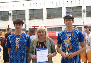Uczniowie oraz nauczyciel wychowania fizycznego z dyplomem, pucharem i medalami.